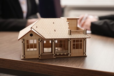 Photo of Real estate agent working with client at desk in office, focus on house model
