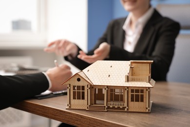 Photo of Real estate agent working with client at desk in office, focus on house model