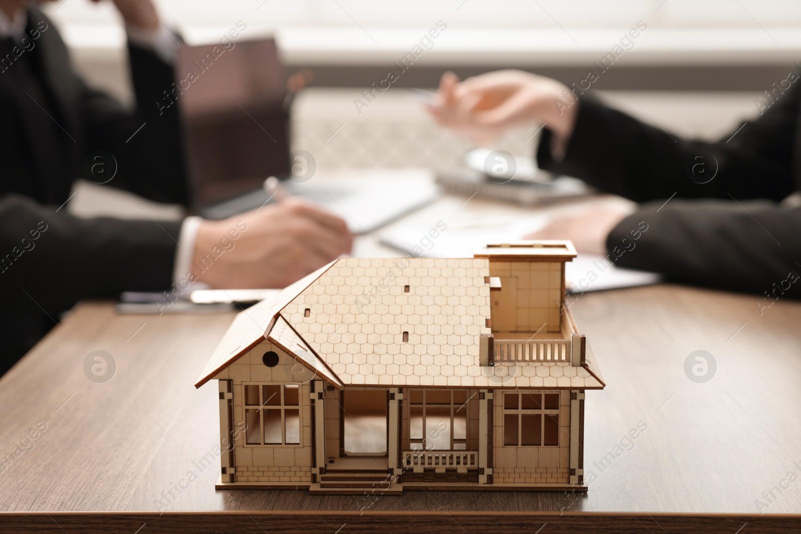 Photo of Real estate agent working with client at desk in office, focus on house model