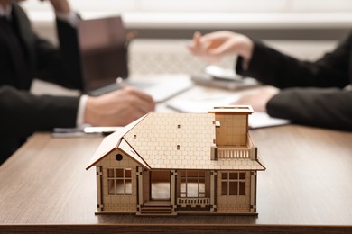 Photo of Real estate agent working with client at desk in office, focus on house model