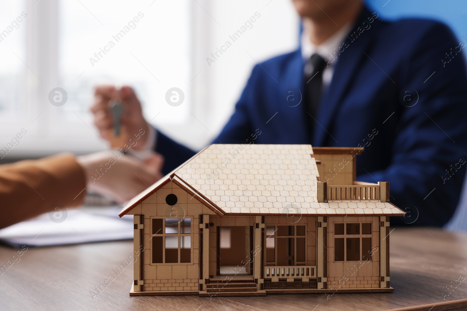 Real estate agent giving key to client at desk in office, focus on house model Photo of Real estate agent giving key to client at desk in office, focus on house model