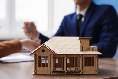 Photo of Real estate agent giving key to client at desk in office, focus on house model