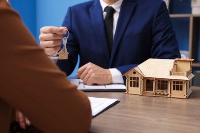 Photo of Real estate agent giving key to client at desk in office, focus on house model