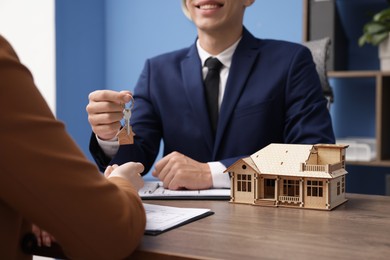 Photo of Real estate agent giving key to client at desk in office, focus on house model