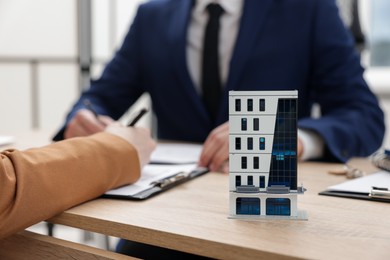 Photo of Real estate agent working with client at desk in office, focus on house model