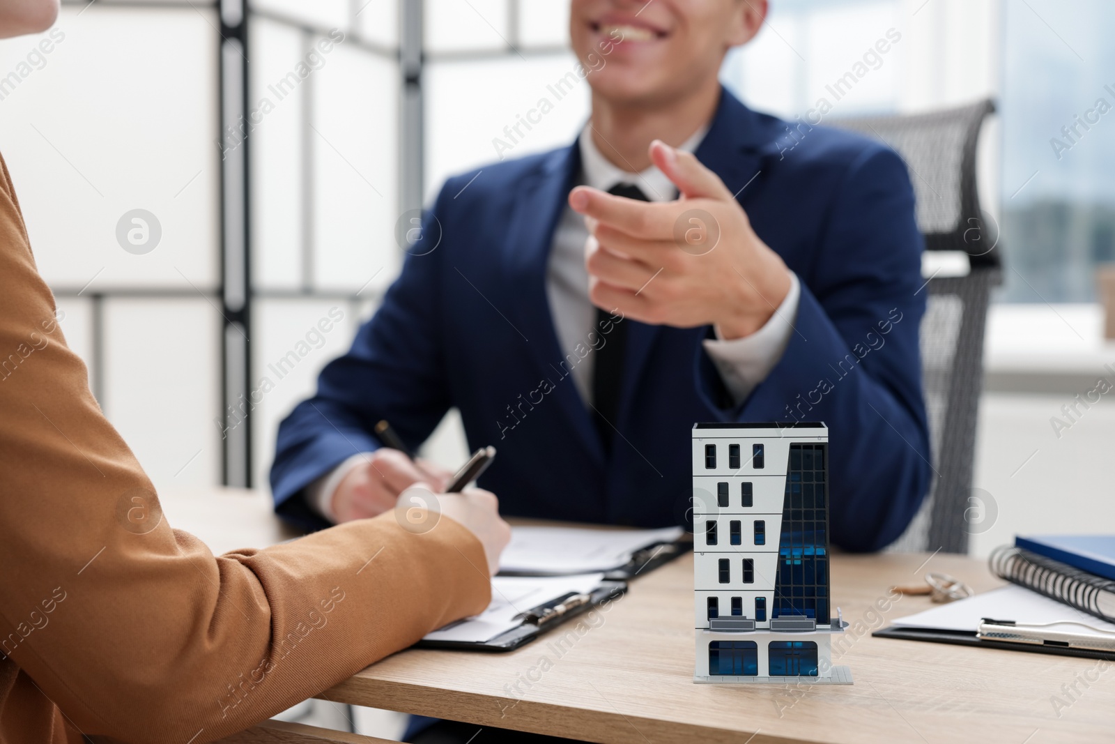 Real estate agent working with client at desk in office, focus on house model Photo of Real estate agent working with client at desk in office, focus on house model