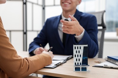 Photo of Real estate agent working with client at desk in office, focus on house model