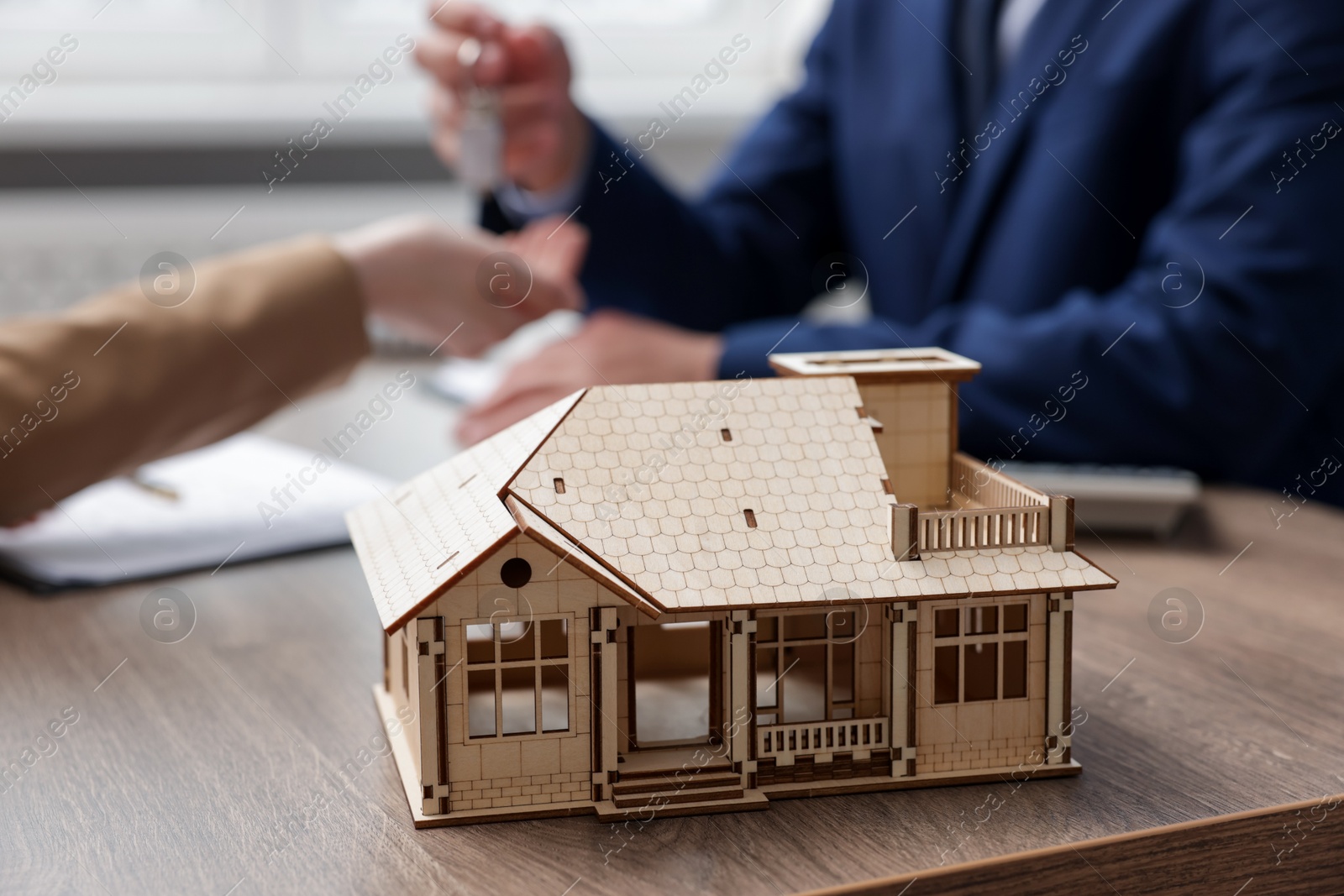 Photo of Real estate agent giving key to client at desk in office, focus on house model