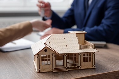Photo of Real estate agent giving key to client at desk in office, focus on house model