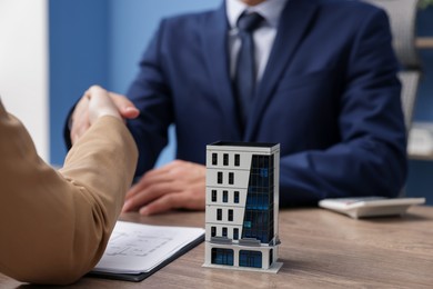 Photo of Real estate agent giving key to client at desk in office, focus on house model