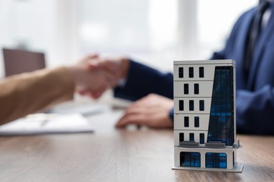 Photo of Real estate agent and client shaking hands at desk in office, focus on house model