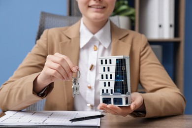 Photo of Real estate agent holding key and house model at desk in office, closeup
