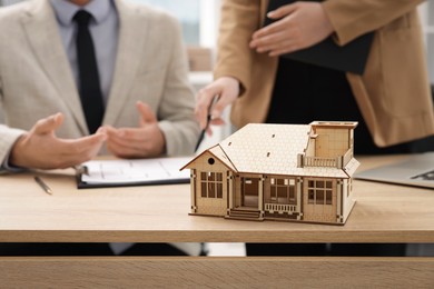 Photo of Real estate agent working with client at desk in office, focus on house model