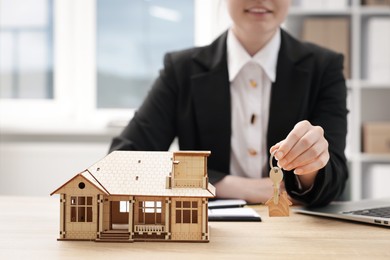 Photo of Real estate agent holding key at desk in office, focus on house model