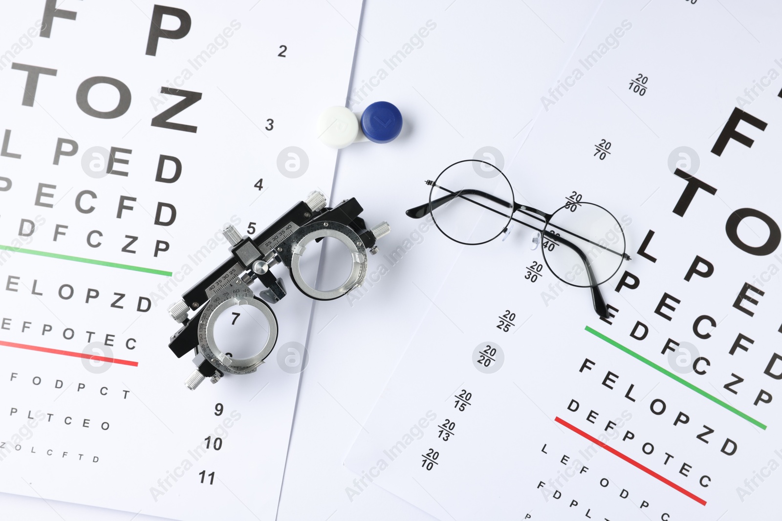 Photo of Vision test charts, glasses, trial frame and lenses on white background, flat lay
