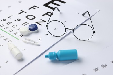 Photo of Vision test chart, glasses, tweezers, bottles of medical drops and lenses on white background, closeup