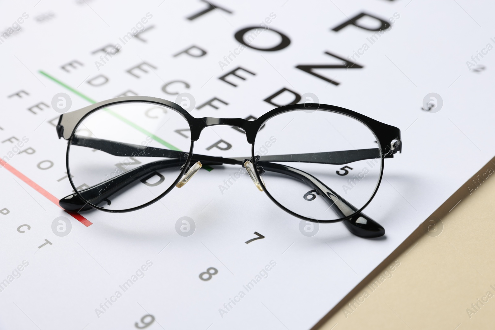 Photo of Vision test chart and glasses on beige background, closeup