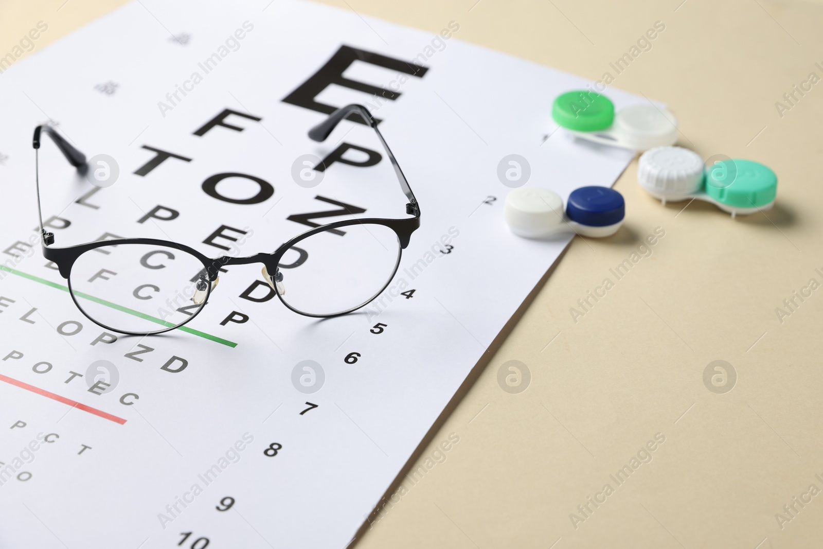 Vision test chart, glasses and lenses on beige background, closeup. Space for text Photo of Vision test chart, glasses and lenses on beige background, closeup. Space for text