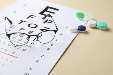 Photo of Vision test chart, glasses and lenses on beige background, closeup. Space for text