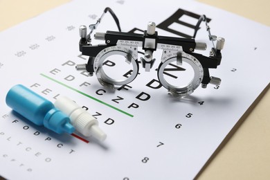 Photo of Vision test chart, trial frame and bottles of medical drops on beige background, closeup
