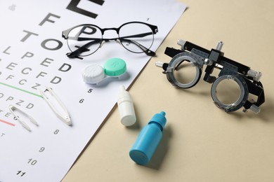 Photo of Vision test chart, trial frame, glasses, lenses, tweezers and bottles of medical drops on beige background, closeup