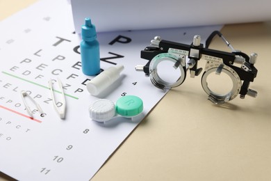 Photo of Vision test chart, trial frame, lenses, tweezers and bottles of medical drops on beige background, closeup