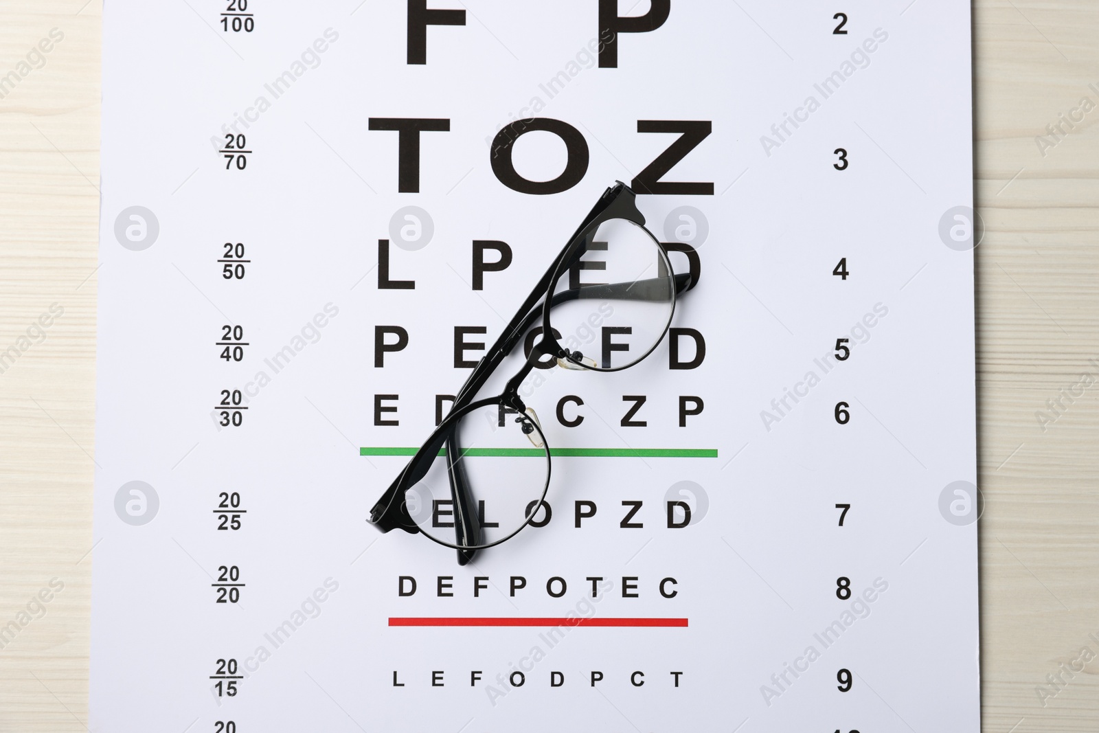Vision test chart and glasses on wooden table, top view Photo of Vision test chart and glasses on wooden table, top view