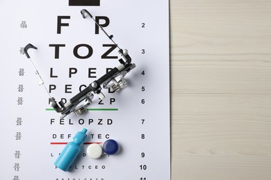 Photo of Vision test chart, trial frame, lenses and bottle of medical drops on wooden table, top view. Space for text