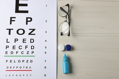 Photo of Vision test chart, glasses, lenses and bottle of medical drops on wooden table, flat lay. Space for text