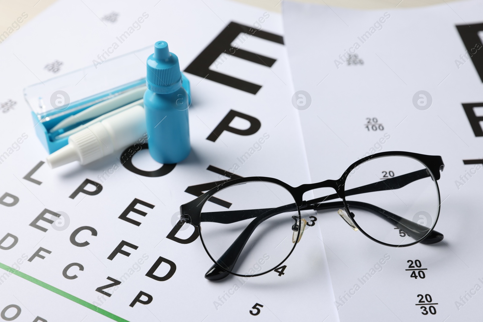Photo of Glasses, bottles of medical drops and tweezers on vision test charts, closeup