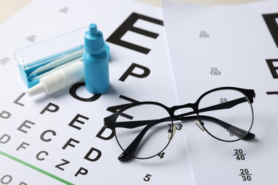Photo of Glasses, bottles of medical drops and tweezers on vision test charts, closeup
