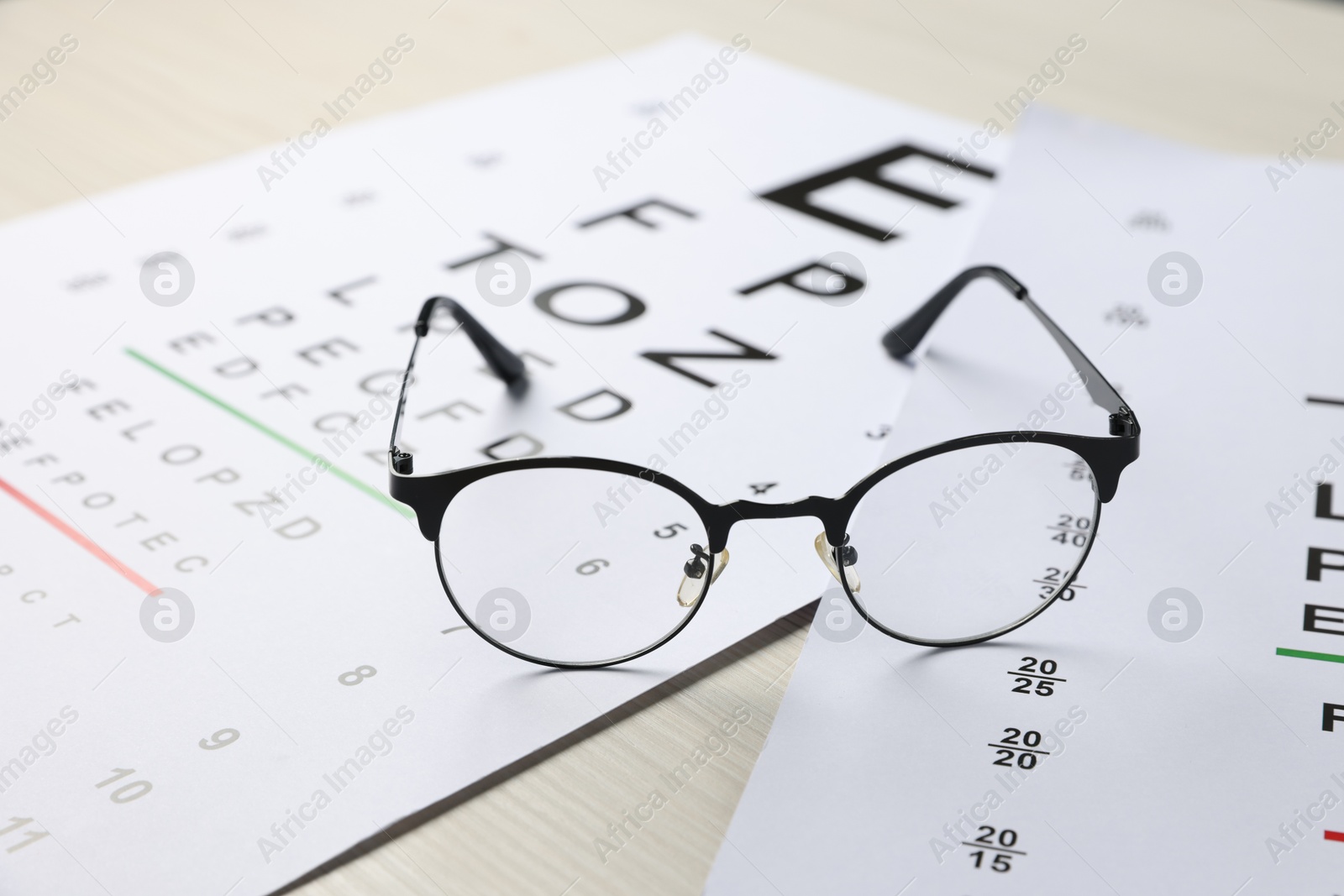Photo of Vision test charts and glasses on wooden table, closeup