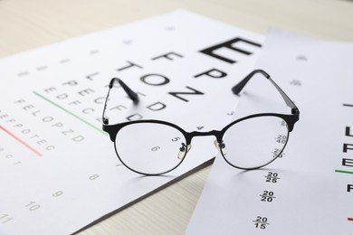 Photo of Vision test charts and glasses on wooden table, closeup