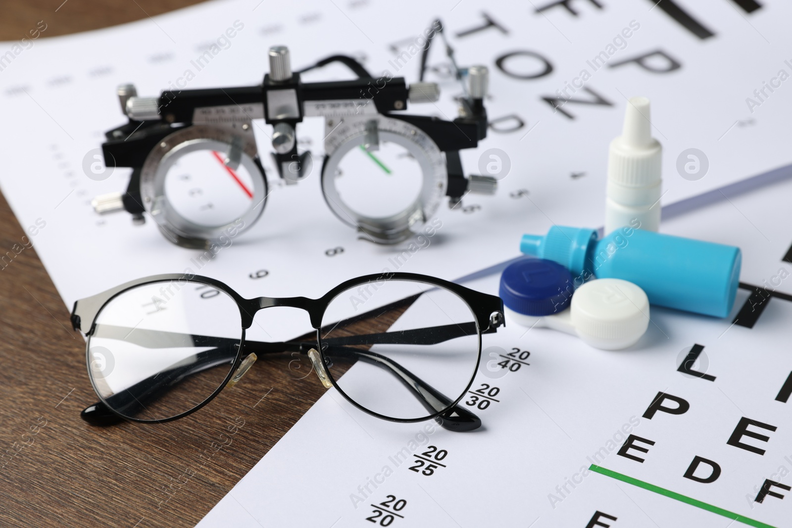 Vision test charts, glasses, trial frame, lenses and bottles of medical drops on wooden table, closeup Photo of Vision test charts, glasses, trial frame, lenses and bottles of medical drops on wooden table, closeup