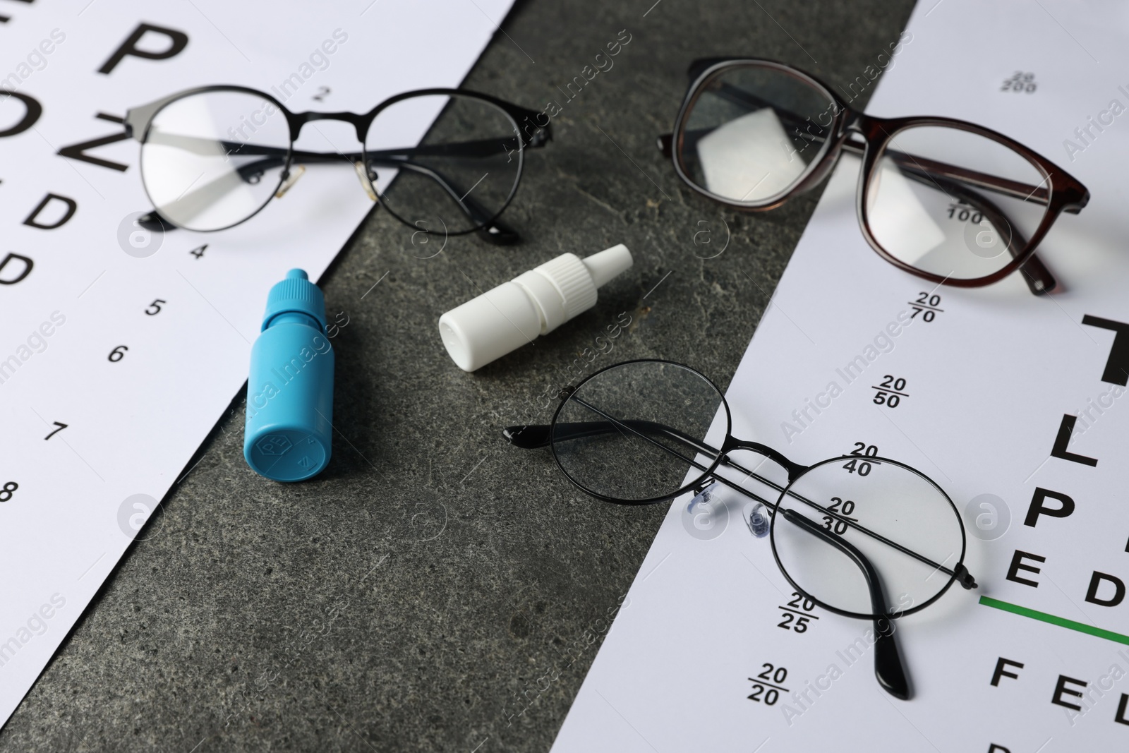 Photo of Vision test charts, bottles of medical drops and glasses on grey table, closeup