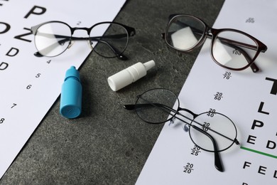 Photo of Vision test charts, bottles of medical drops and glasses on grey table, closeup