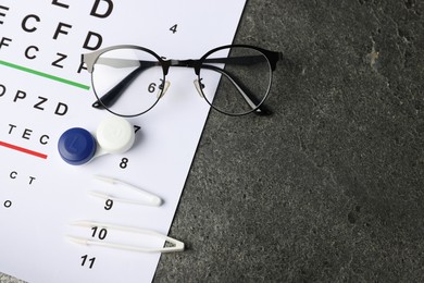 Photo of Vision test chart, glasses, tweezers and lenses on grey table, flat lay. Space for text