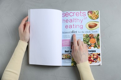 Photo of Woman reading magazine at light grey table, top view. Mockup for design