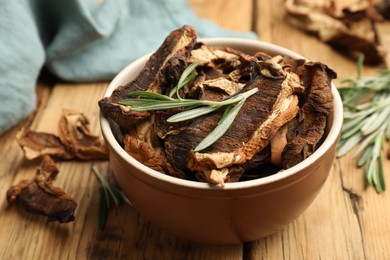 Photo of Dried chanterelle mushrooms with rosemary on wooden table, closeup