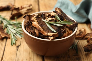 Photo of Dried chanterelle mushrooms with rosemary on wooden table, closeup