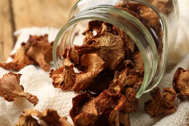Photo of Dried chanterelle mushrooms in jar and towel on wooden table, closeup