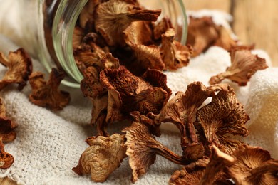 Photo of Dried chanterelle mushrooms in jar and towel on wooden table, closeup