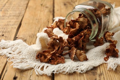 Photo of Dried chanterelle mushrooms in jar and towel on wooden table, closeup. Space for text