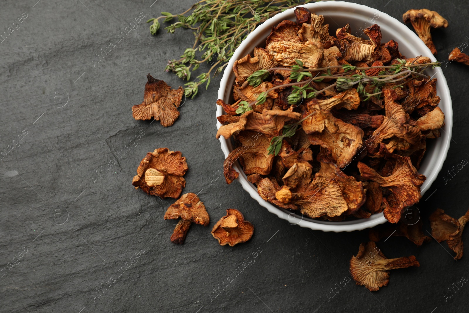Photo of Dried chanterelle mushrooms with thyme on black table, flat lay. Space for text