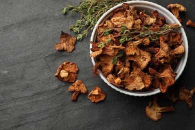 Photo of Dried chanterelle mushrooms with thyme on black table, flat lay. Space for text