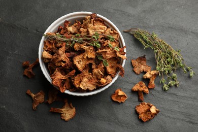 Photo of Dried chanterelle mushrooms with thyme on black table, flat lay