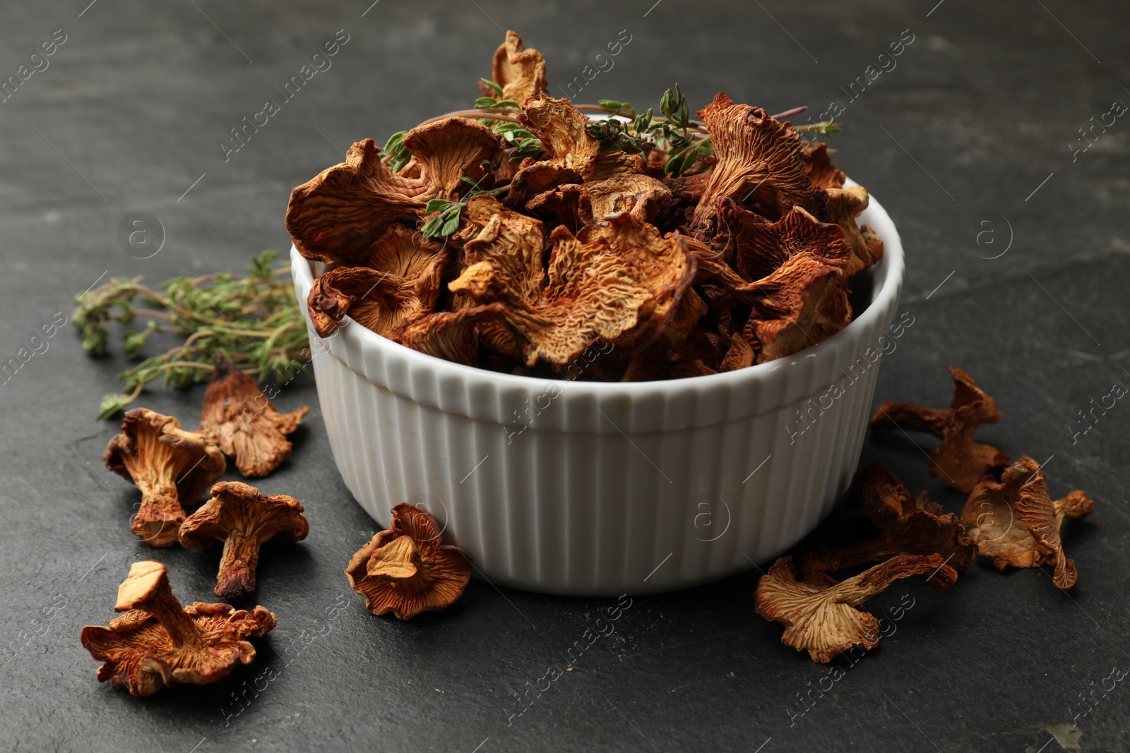 Dried chanterelle mushrooms with thyme on black table, closeup Photo of Dried chanterelle mushrooms with thyme on black table, closeup