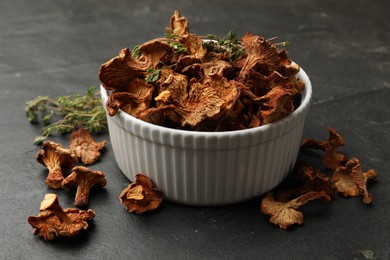 Photo of Dried chanterelle mushrooms with thyme on black table, closeup