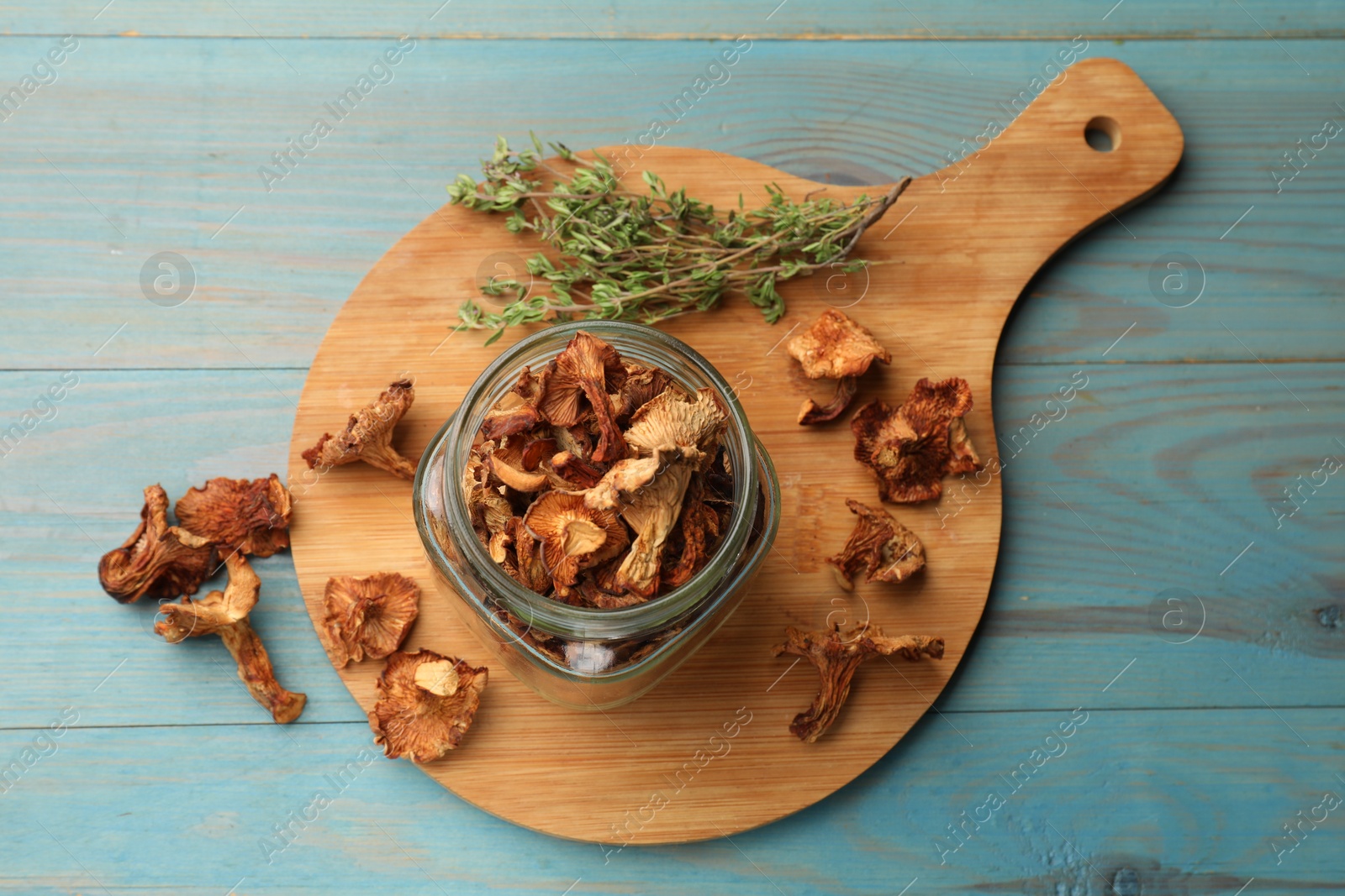 Photo of Dried chanterelle mushrooms with thyme on blue wooden table, top view