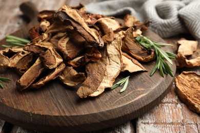 Photo of Dried chanterelle mushrooms with rosemary on wooden table, closeup